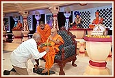Swamishri holds a walking stick, mala and bouquet for an aged devotee as he stands up