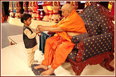 Swamishri gives a small garland to a child who wandered onto the stage